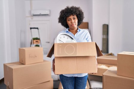 Photo for Black woman with curly hair moving to a new home holding cardboard box relaxed with serious expression on face. simple and natural looking at the camera. - Royalty Free Image