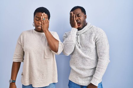 Photo for Young african american couple standing over blue background together yawning tired covering half face, eye and mouth with hand. face hurts in pain. - Royalty Free Image