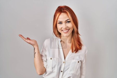 Photo for Young caucasian woman standing over isolated background smiling cheerful presenting and pointing with palm of hand looking at the camera. - Royalty Free Image