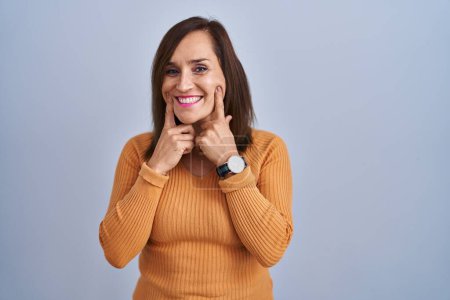 Téléchargez les photos : Middle age brunette woman standing wearing orange sweater smiling with open mouth, fingers pointing and forcing cheerful smile - en image libre de droit