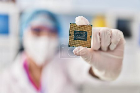 Photo for Young beautiful hispanic woman scientist wearing medical mask holding cpu processor chip at pharmacy - Royalty Free Image