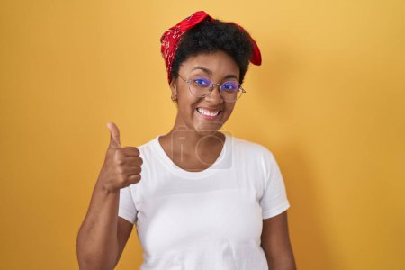 Photo for Young african american woman standing over yellow background doing happy thumbs up gesture with hand. approving expression looking at the camera showing success. - Royalty Free Image