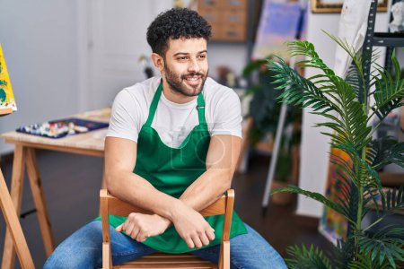 Photo for Young arab man artist smiling confident sitting on chair at art studio - Royalty Free Image