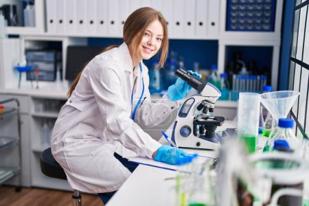 Téléchargez les photos : Young caucasian woman scientist using microscope write on document at laboratory - en image libre de droit