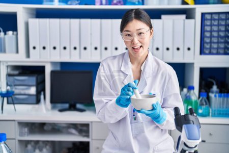 Photo for Chinese young woman working at scientist laboratory mixing smiling and laughing hard out loud because funny crazy joke. - Royalty Free Image