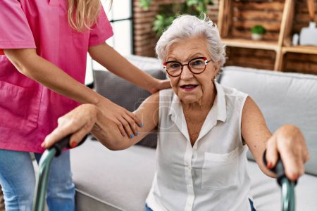Téléchargez les photos : Patiente âgée aux cheveux gris soutenue par une infirmière et une marchette en gériatrie - en image libre de droit