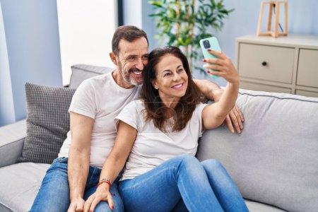 Foto de Mediana edad hombre y mujer pareja hacer selfie por el teléfono inteligente sentado en el sofá en casa - Imagen libre de derechos