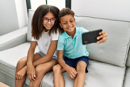 Foto de Hermano y hermana hacen selfie por el teléfono inteligente sentado en el sofá en casa - Imagen libre de derechos