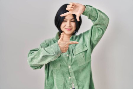Photo for Young asian woman standing over white background smiling making frame with hands and fingers with happy face. creativity and photography concept. - Royalty Free Image
