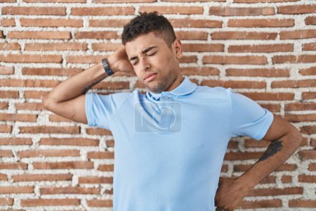 Photo for Brazilian young man standing over brick wall stretching back, tired and relaxed, sleepy and yawning for early morning - Royalty Free Image