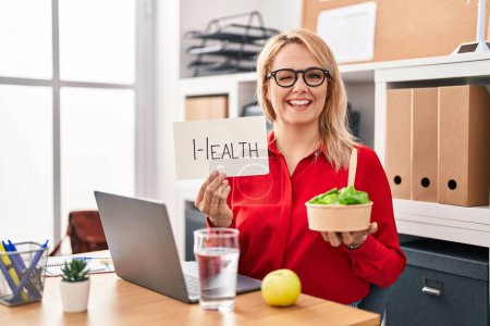 Photo for Blonde woman working at the office eating healthy food winking looking at the camera with sexy expression, cheerful and happy face. - Royalty Free Image
