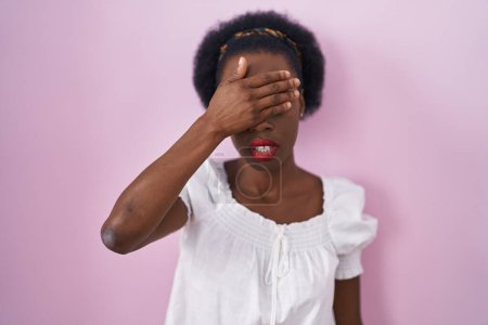 Photo for African woman with curly hair standing over pink background covering eyes with hand, looking serious and sad. sightless, hiding and rejection concept - Royalty Free Image