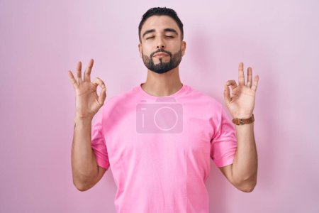 Photo for Hispanic young man standing over pink background relaxed and smiling with eyes closed doing meditation gesture with fingers. yoga concept. - Royalty Free Image
