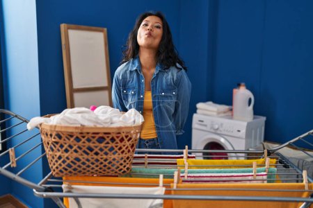 Foto de Young asian woman hanging clothes at clothesline making fish face with lips, crazy and comical gesture. funny expression. - Imagen libre de derechos
