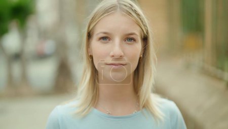 Téléchargez les photos : Jeune femme blonde debout avec une expression sérieuse dans la rue - en image libre de droit
