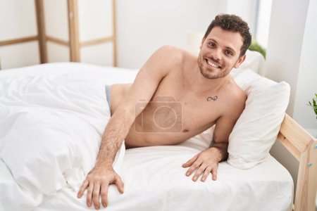 Téléchargez les photos : Jeune homme hispanique souriant confiant couché sur le lit dans la chambre - en image libre de droit