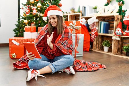 Photo for Young hispanic girl having video call sitting by christmas tree at home. - Royalty Free Image