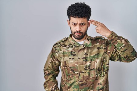 Foto de Hombre árabe vistiendo camuflaje uniforme del ejército disparando y matándose apuntando de la mano y los dedos a la cabeza como arma, gesto suicida. - Imagen libre de derechos
