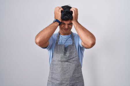 Photo for Hispanic young man wearing apron over white background suffering from headache desperate and stressed because pain and migraine. hands on head. - Royalty Free Image