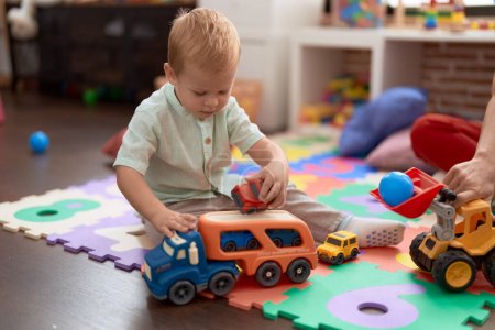 Téléchargez les photos : Adorable toddler playing with car toy sitting on floor at kindergarten - en image libre de droit