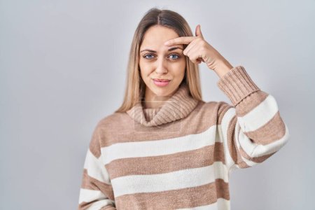 Photo for Young blonde woman wearing turtleneck sweater over isolated background pointing unhappy to pimple on forehead, ugly infection of blackhead. acne and skin problem - Royalty Free Image