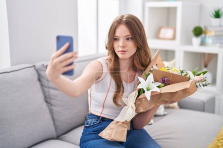 Téléchargez les photos : Femme blanche tenant un bouquet de fleurs blanches prenant une photo selfie détendue avec une expression sérieuse sur le visage. simple et naturel regardant la caméra. - en image libre de droit