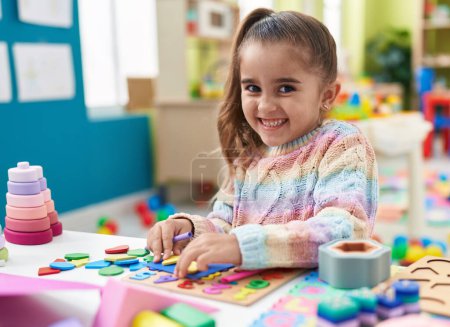 Foto de Adorable chica hispana jugando con matemáticas juego de puzzle de pie en el jardín de infantes - Imagen libre de derechos