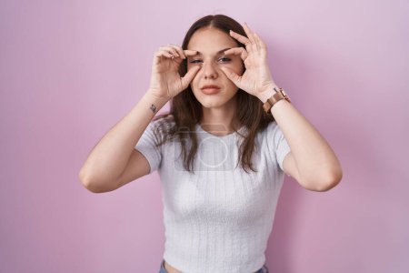 Téléchargez les photos : Young hispanic girl standing over pink background trying to open eyes with fingers, sleepy and tired for morning fatigue - en image libre de droit