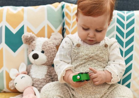 Téléchargez les photos : Adorable rousse tout-petit jouant avec jouet de voiture assis sur le canapé à la maison - en image libre de droit