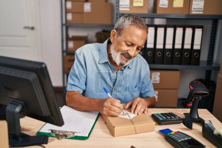 Téléchargez les photos : Senior homme aux cheveux gris ecommerce travailleur d'affaires écrivant sur le paquet au bureau - en image libre de droit