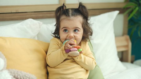 Téléchargez les photos : Adorable hispanic girl sucking toy sitting on bed at bedroom - en image libre de droit