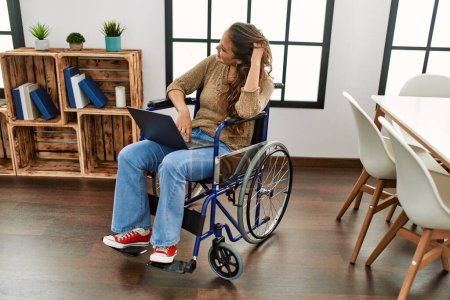 Photo for Young beautiful hispanic woman using laptop sitting on wheelchair at home - Royalty Free Image
