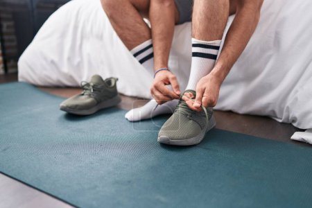 Photo for Young hispanic man tying sneaker at bedroom - Royalty Free Image