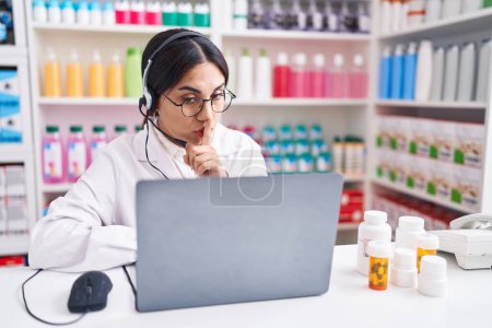 Téléchargez les photos : Young arab woman working at pharmacy drugstore using laptop asking to be quiet with finger on lips. silence and secret concept. - en image libre de droit