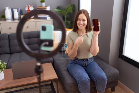 Téléchargez les photos : Belle femme brune enregistrement tutoriel vlog avec smartphone à la maison souriant heureux pointage avec la main et le doigt - en image libre de droit
