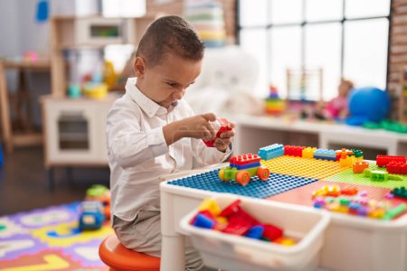 Foto de Adorable niño jugando con bloques de construcción sentado en la mesa en el jardín de infantes - Imagen libre de derechos