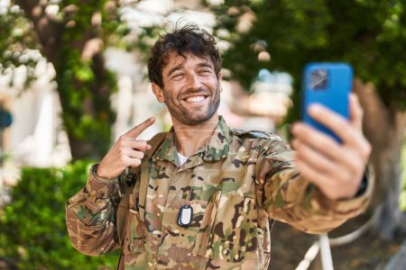 Foto de Hispanic young man wearing camouflage army uniform doing video call smiling happy pointing with hand and finger - Imagen libre de derechos