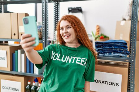 Téléchargez les photos : Jeune rousse femme portant un uniforme bénévole faire selfie par le smartphone au centre de charité - en image libre de droit