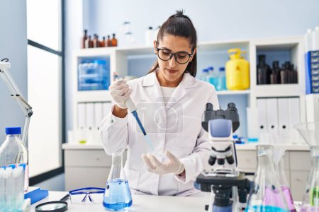 Photo for Young hispanic woman wearing scientist uniform using pipette working at laboratory - Royalty Free Image