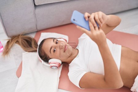 Photo for Young beautiful hispanic woman listening to music lying on yoga mat at home - Royalty Free Image