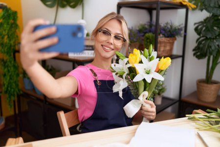 Photo for Young blonde woman florist make selfie by smartphone holding flowers at flower shop - Royalty Free Image
