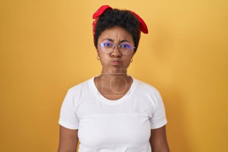 Photo for Young african american woman standing over yellow background puffing cheeks with funny face. mouth inflated with air, crazy expression. - Royalty Free Image