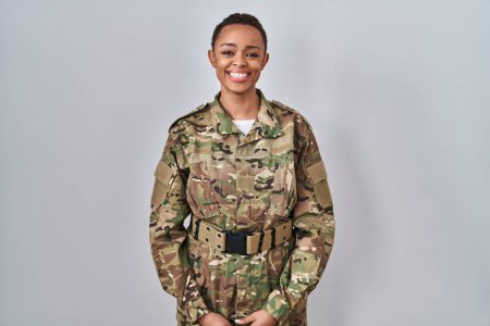 Foto de Hermosa mujer afroamericana vistiendo uniforme camuflaje del ejército con una sonrisa feliz y fresca en la cara. persona afortunada. - Imagen libre de derechos