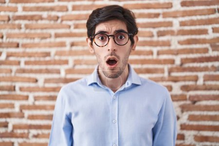 Téléchargez les photos : Young hispanic man standing over brick wall background afraid and shocked with surprise and amazed expression, fear and excited face. - en image libre de droit