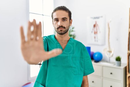 Photo for Young physiotherapist working at pain recovery clinic doing stop sing with palm of the hand. warning expression with negative and serious gesture on the face. - Royalty Free Image