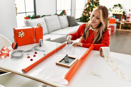 Téléchargez les photos : Jeune femme caucasienne préparant cadeau assis par arbre de Noël à la maison - en image libre de droit