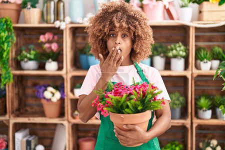Photo for Young hispanic woman with curly hair working at florist shop holding plant covering mouth with hand, shocked and afraid for mistake. surprised expression - Royalty Free Image