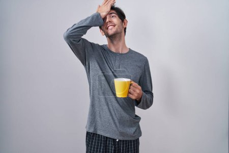 Photo for Young hispanic man wearing pajama drinking a cup of coffee surprised with hand on head for mistake, remember error. forgot, bad memory concept. - Royalty Free Image