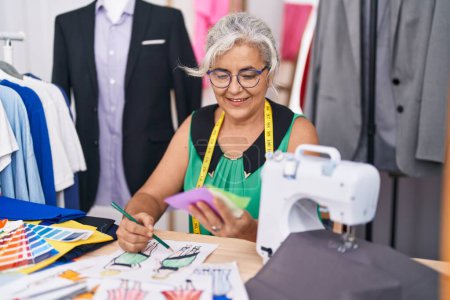 Foto de Mediana edad gris mujer sastre celebración tela dibujo ropa diseño en sastrería - Imagen libre de derechos