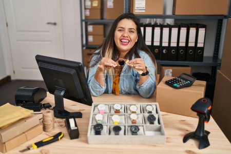 Foto de Mujer hispana joven que trabaja en el comercio electrónico de pequeñas empresas vendiendo relojes sonriendo y riendo en voz alta porque divertida broma loca. - Imagen libre de derechos